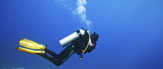 Scuba diver swimming under water and examines the seabed